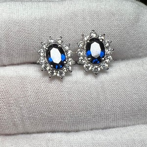 Puede incluir: Un par de pendientes de plata con una piedra ovalada azul rodeada de piedras peque&ntilde;as transparentes.