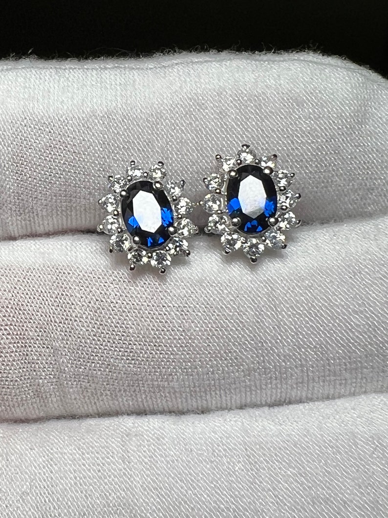 Puede incluir: Un par de pendientes de plata con una piedra ovalada azul rodeada de piedras peque&ntilde;as transparentes.