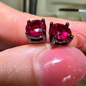 Könnte beinhalten: Ein Paar schwarze Ohrstecker mit runden, leuchtend roten Edelsteinen.