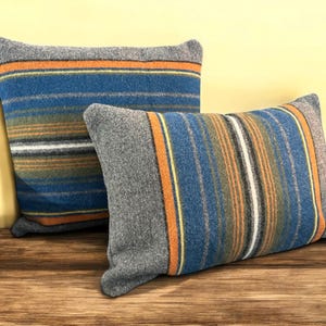 May include: Two decorative throw pillows with a striped pattern in shades of blue, orange, green, and gray. The pillows are made of a soft, textured fabric.