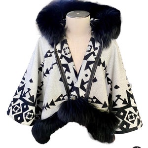 May include: A white and black patterned cape with a black fur-lined hood and trim. The cape features a geometric design and is displayed on a mannequin. The cape is a stylish outerwear garment.