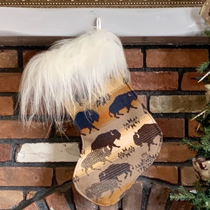 May include: A brown and tan Christmas stocking with a white faux fur cuff. The stocking features a repeating pattern of brown and black buffalo silhouettes.