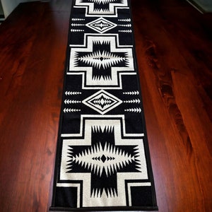May include: Black and white geometric patterned table runner with a southwestern design. The runner is on a dark wood table.