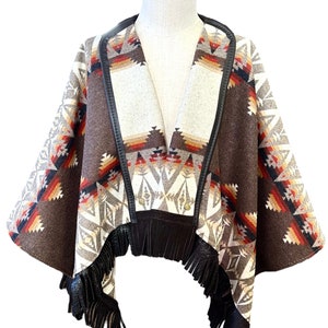 May include: A brown and white patterned poncho with black leather trim and fringe. The poncho has a geometric design with red, orange, and yellow accents.