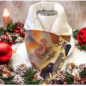 Peut inclure: Un tour de cou en polaire à motif brun, beige et bleu avec une doublure en fausse fourrure blanche. Le tour de cou est présenté sur une surface blanche avec un fond sur le thème de Noël.