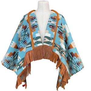 May include: A turquoise poncho with a geometric pattern in brown, white, and green. The poncho has brown leather fringe and trim. The garment is displayed on a mannequin.