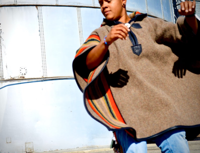 May include: A person wearing a brown poncho with colorful stripes and blue jeans. The poncho has a dark blue trim and a decorative buckle.