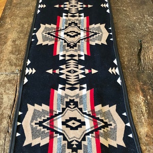 May include: Black table runner with a geometric pattern in shades of brown, white, red, and gray. The pattern is reminiscent of Native American designs.