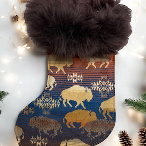 May include: A brown faux fur stocking with a blue and brown buffalo plaid pattern. The stocking is decorated with a repeating pattern of buffalo silhouettes.