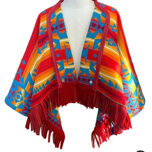 Puede incluir: Un poncho rojo, naranja, amarillo, azul y blanco con estampado, con ribete de cuero y flecos. El poncho tiene un cierre de botón.