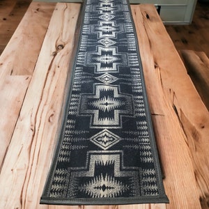 Op de afbeelding: Een zwart-witte tafelrunner met een geometrisch patroon. De runner ligt op een houten tafel.