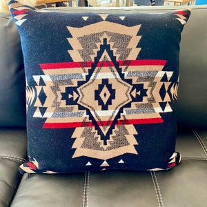 May include: A black throw pillow with a geometric pattern in shades of brown, red, and white. The pattern features a central diamond shape with triangles and stripes.