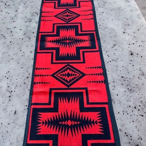 May include: Red and black table runner with a geometric pattern. The pattern features a repeating design of crosses and diamonds.