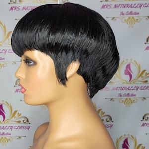 May include: A black short pixie wig with a side part and a pin on top. The wig is styled with a short, choppy fringe and layers. The wig is on a mannequin head.