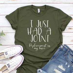 May include: A green t-shirt with the text "I just had a joint replacement in my knee" printed in white.