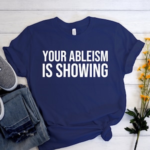 May include: A navy blue t-shirt with white text that reads "Your ableism is showing".