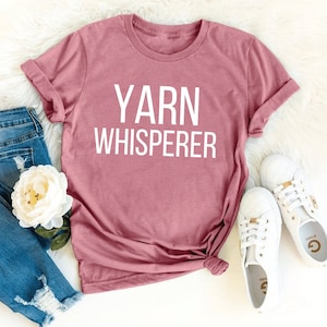 May include: A pink t-shirt with the text "YARN WHISPERER" in white lettering.