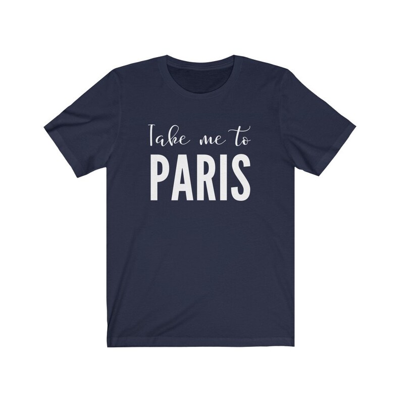 May include: A navy blue short-sleeved t-shirt featuring the white printed text "Take me to PARIS" centered on the chest. The design combines a cursive script font for the words "Take me to" positioned above the bold, capitalized word "PARIS".