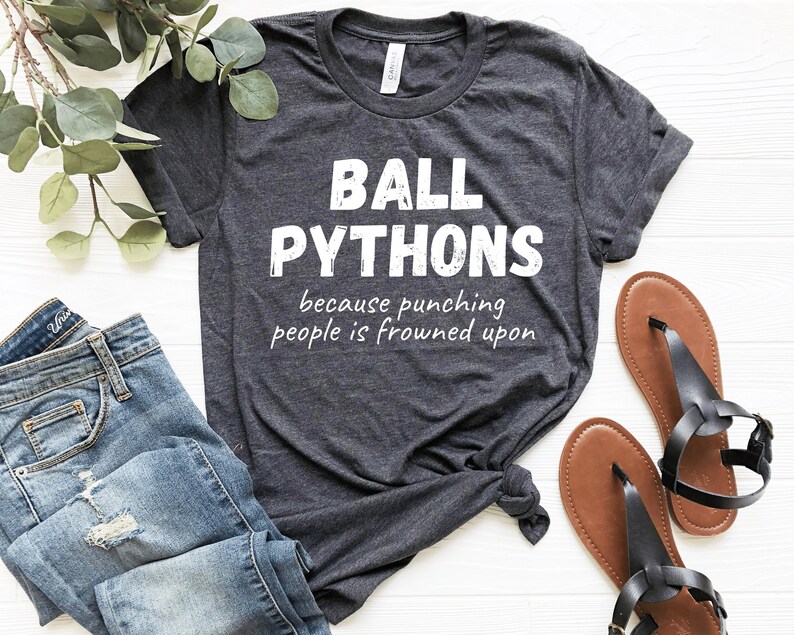 May include: Dark gray t-shirt with the text "BALL PYTHONS" above the phrase "because punching people is frowned upon" in white. The shirt is paired with blue jeans and brown sandals.