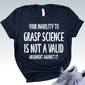 May include: Navy blue t-shirt with the white text: "YOUR INABILITY TO GRASP SCIENCE IS NOT A VALID ARGUMENT AGAINST IT." The shirt has short sleeves and a crew neck.