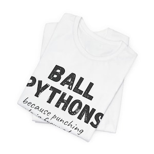 May include: White t-shirts with the text "BALL PYTHONS" in large, black, distressed font. The text "because punching..." is below. The shirts are folded and stacked on top of each other.