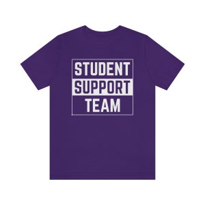 Może przedstawiać: Fioletowy T-shirt z białym tekstem, kt&oacute;ry brzmi "STUDENT SUPPORT TEAM" w ramce.