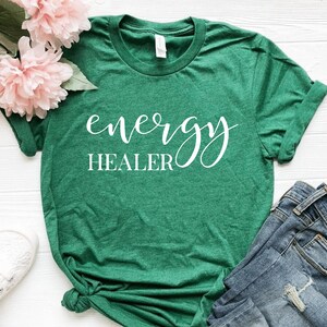 Pode incluir: Camiseta verde com texto branco que diz "energy healer" em fonte cursiva.