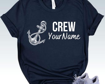 May include: A navy blue short-sleeved t-shirt featuring a white graphic of an anchor wrapped in rope on the left side. The text "CREW" is printed in a bold white sans-serif font above the white cursive script text "YourName" on the right.