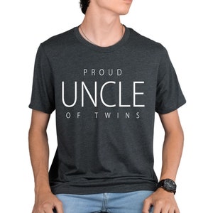 May include: A dark gray t-shirt with white text that reads "Proud Uncle of Twins".