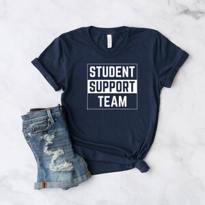 Może przedstawiać: Koszulka w kolorze granatowym z białym napisem "STUDENT SUPPORT TEAM" w ramce.