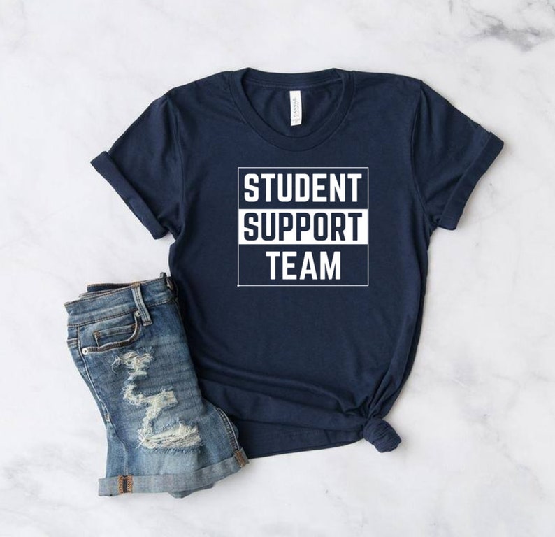 Może przedstawiać: Koszulka w kolorze granatowym z białym napisem "STUDENT SUPPORT TEAM" w ramce.