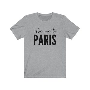 May include: A heather gray short-sleeve t-shirt featuring the text Take me to PARIS printed in black across the chest. The words Take me to are in a cursive script font, while the word PARIS is in a bold, uppercase sans-serif typeface.