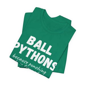May include: A folded green t-shirt with the words "BALL PYTHONS" in large white block letters. Below, smaller text reads "because punching is frowned upon." The shirt is made of a soft material.