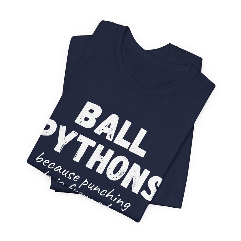 May include: Navy blue t-shirt with the text "BALL PYTHONS" in large white letters. Below the text is the phrase "because punching is frowned upon". The shirt is folded.