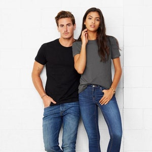 May include: Two people wearing plain t-shirts, one black and one gray, standing against a white brick wall. Both are wearing blue jeans.