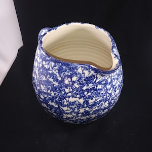 May include: A blue and white ceramic pitcher with a speckled glaze. The pitcher has a wide mouth and a handle.