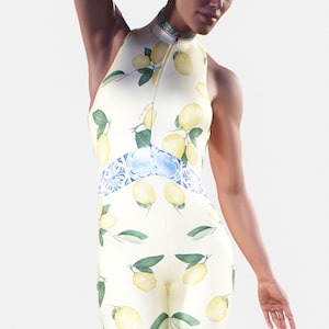 Könnte beinhalten: Ein weißer Jumpsuit mit Zitronenprint und einem blauen und weißen gemusterten Band um die Taille. Der Jumpsuit hat einen hohen Kragen und einen Reißverschluss vorne. Die Worte "BOOTY GORE" sind auf den Beinen unten aufgedruckt.