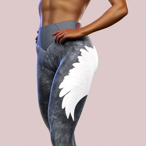 Könnte beinhalten: Graue und weiße Leggings mit einem weißen Flügeldesign am rechten Bein. Die Leggings sind aus dehnbarem Material und haben einen hohen Bund.