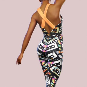 May include: Black one-piece jumpsuit with a colourful cassette tape pattern. The jumpsuit has a criss-cross strap design at the back.