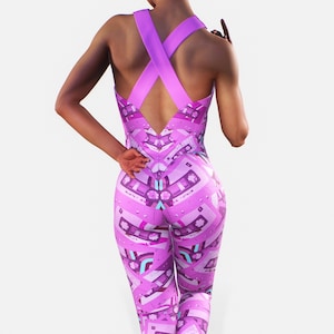 Könnte beinhalten: Ein pinkfarbener und violetter Jumpsuit mit einem Kassettenband-Muster. Der Jumpsuit hat einen gekreuzten Rücken und eine körpernahe Passform. Das Model wird von hinten gezeigt, ein Arm an der Seite, der andere erhoben. Das Muster wiederholt sich.