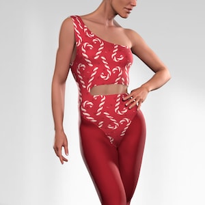 May include: A one-shoulder bodysuit with a candy cane pattern on the top and solid red leggings. The bodysuit has a cutout at the waist. The outfit is a festive holiday design.