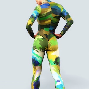 May include: A full-body jumpsuit featuring a colourful, abstract design in green, blue, yellow, and brown. The long-sleeved jumpsuit has a high collar and a close-fitting design. The model is standing with hands on hips.
