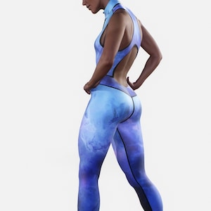 Könnte beinhalten: Ein einteiliger Sport-Jumpsuit in Blau- und Lilatönen mit einem aquarellartigen Muster. Der Jumpsuit hat einen hohen Kragen, einen offenen Rücken und eine figurbetonte Silhouette. Schwarze Zierleisten akzentuieren die Nähte und Kanten des Jumpsuits.
