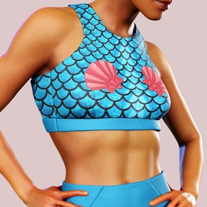 Puede incluir: Un conjunto de top corto y leggings azul con un patrón de escamas de sirena y detalles de conchas rosas.