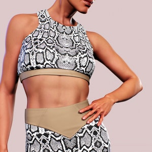 Op de afbeelding: Een zwarte en witte slangenprint sportbeha en leggings set met een tan gekleurde tailleband.