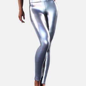 May include: High-waisted leggings in a metallic silver finish with a smooth, reflective surface. These form-fitting trousers feature a wide waistband with visible vertical seam detailing along the front and a sleek, streamlined silhouette.
