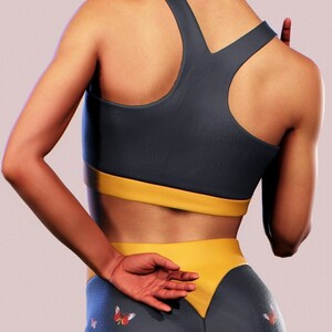 May include: A dark blue and yellow sports bra and leggings set with a butterfly print. The leggings have a yellow waistband and a V-shaped yellow panel at the back.