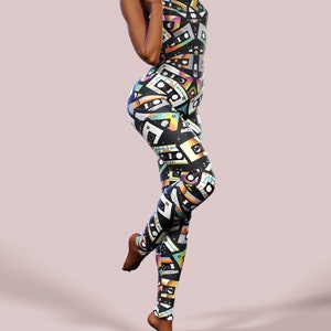 May include: A black jumpsuit with a colourful retro cassette tape pattern. The jumpsuit has a sleeveless design and a high neckline.