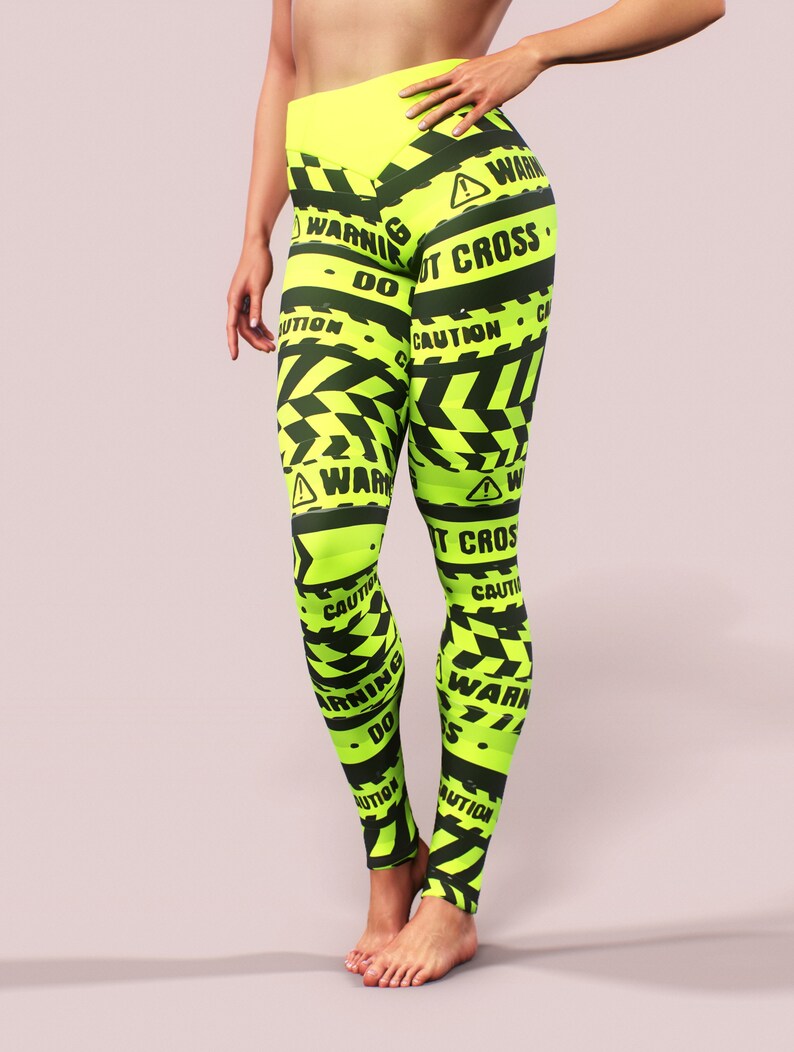 May include: Neon green leggings with black warning tape design. The leggings feature the words "WARNING", "CAUTION", and "DO NOT CROSS" in black. The high-waisted leggings are made of a stretchy material.