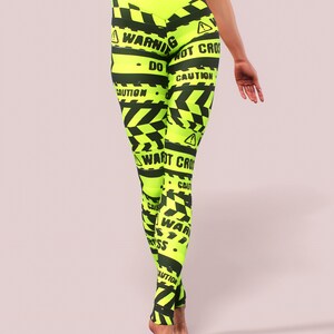 May include: Neon yellow leggings with black caution tape design and the words "WARNING", "DO NOT CROSS", and "CAUTION". The high-waisted leggings are form-fitting and made of a stretchy material.
